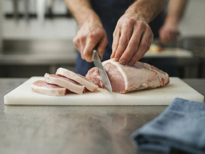 Slager snijdt een varkensrug in dikke karbonades op een witte snijplank